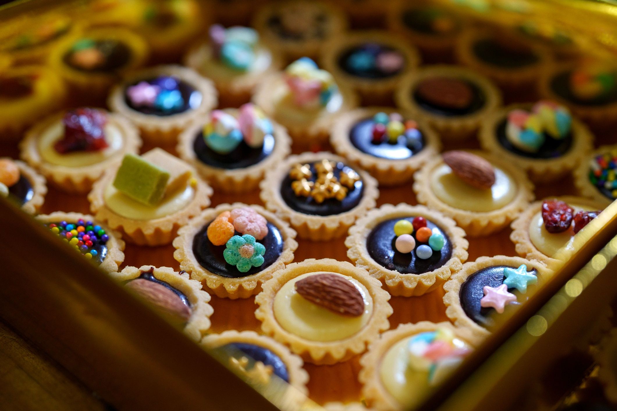Mini tarts with colorful toppings arranged in a gold box