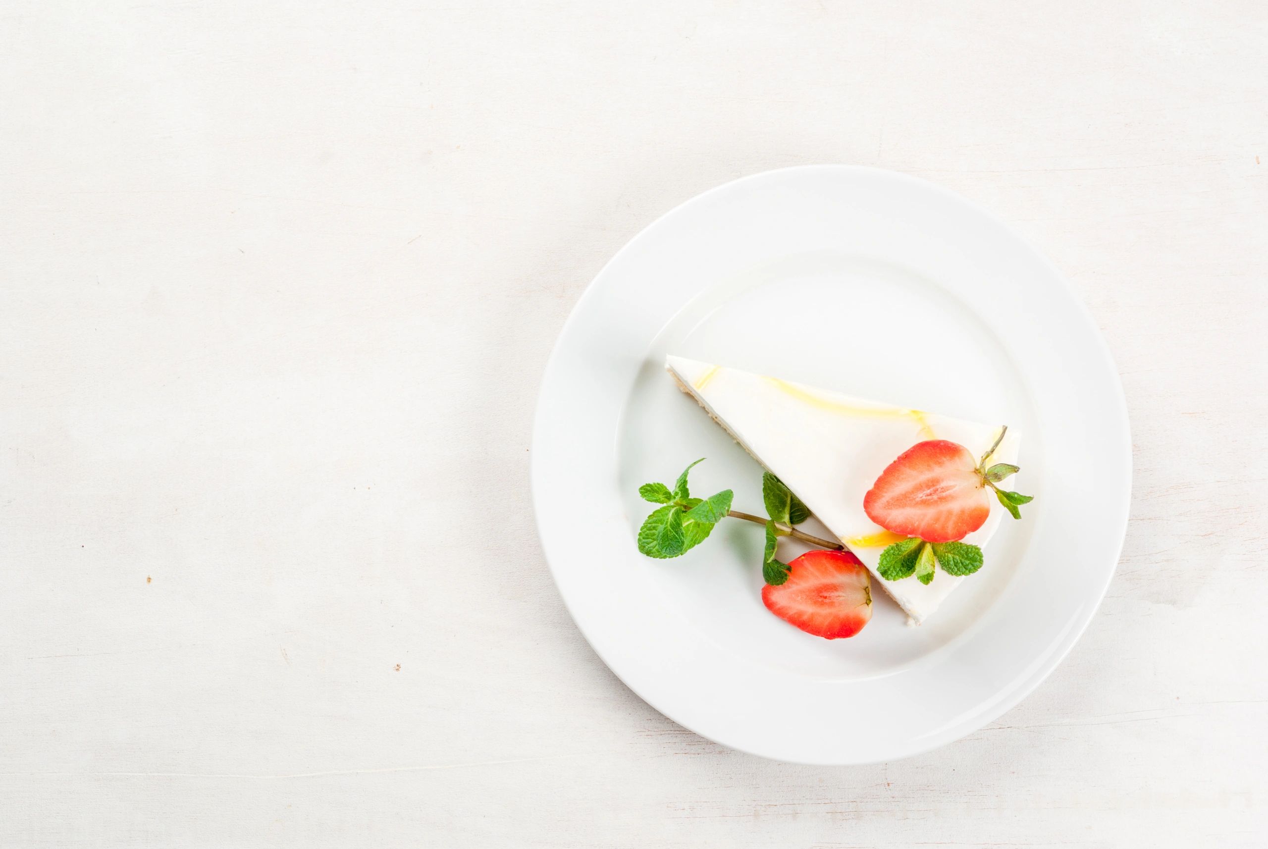 Cheesecake topped with strawberries and mint on a white plate